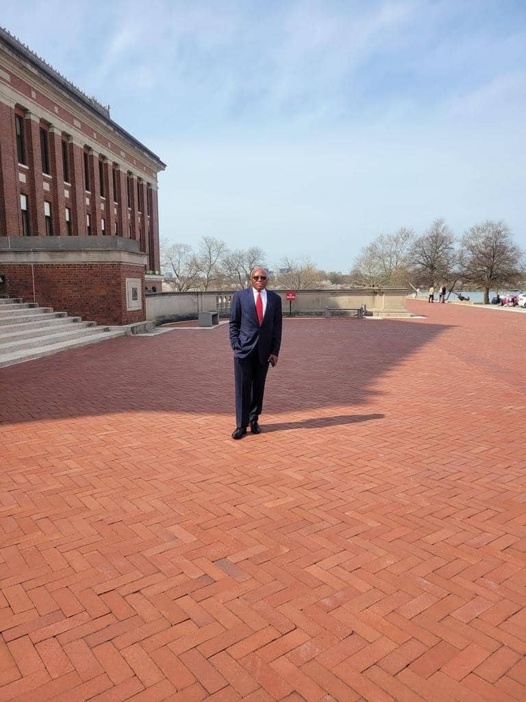 A man standing beside a large brick building and plaza