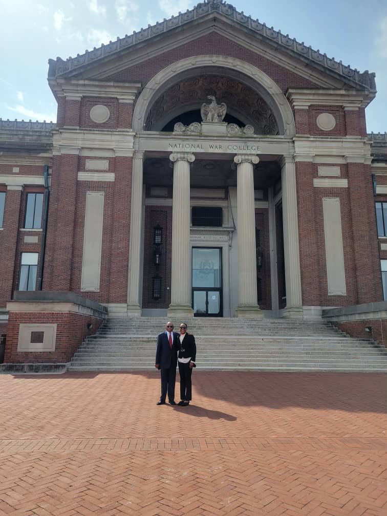 Two people posing together outside a brick building