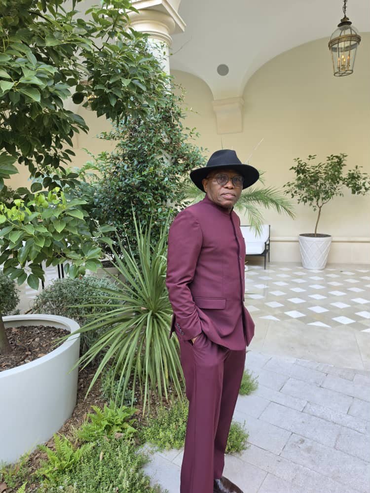 A man in a burgundy outfit standing in a courtyard