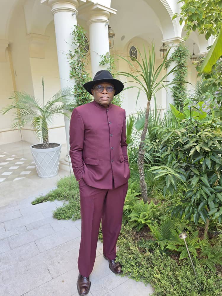 A man in a burgundy outfit standing among garden plants