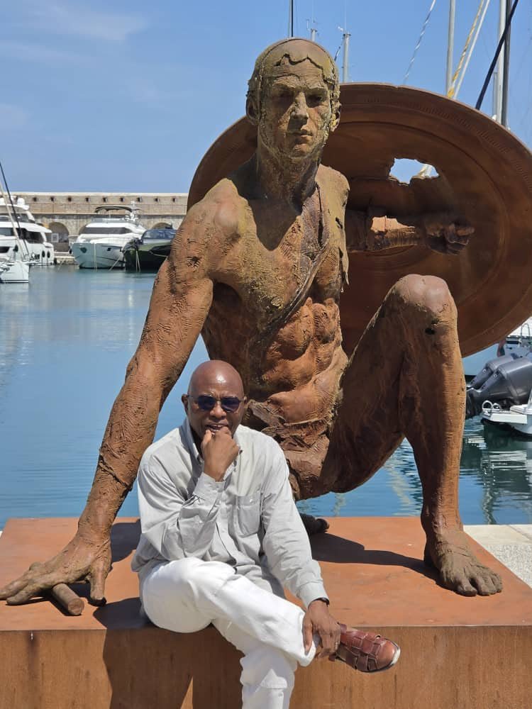 A man seated beside a large sculpture outdoors