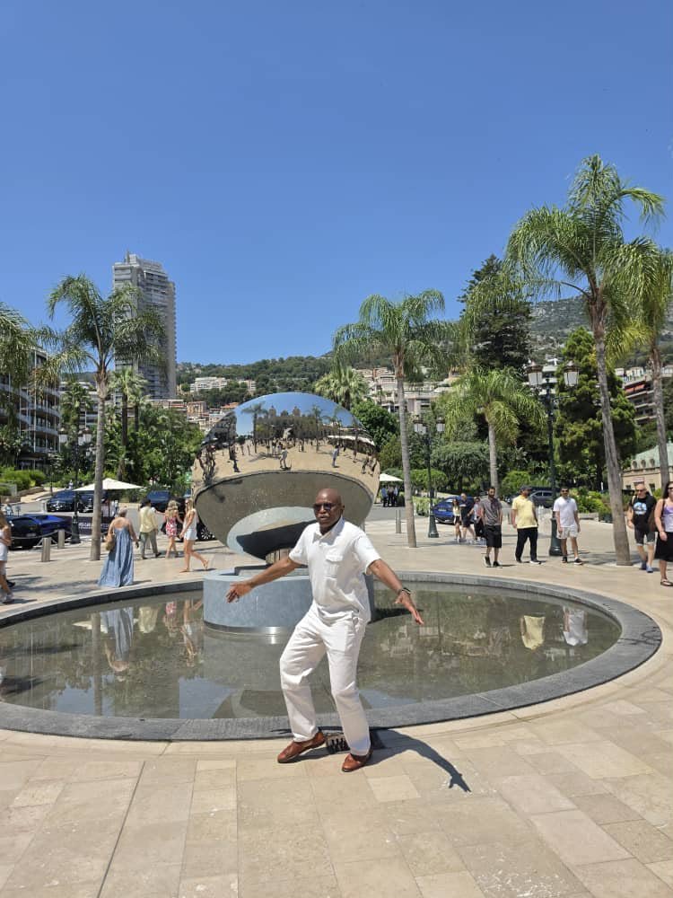A man in light clothing by a fountain in a sunny plaza